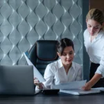 young business lady female director sitting office desk with documents working process business meeting working with colleague solving business tasks office collective concept 1